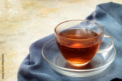 freshly brewed black tea in a glass cup, steaming hot drink on a blue napkin, copy space