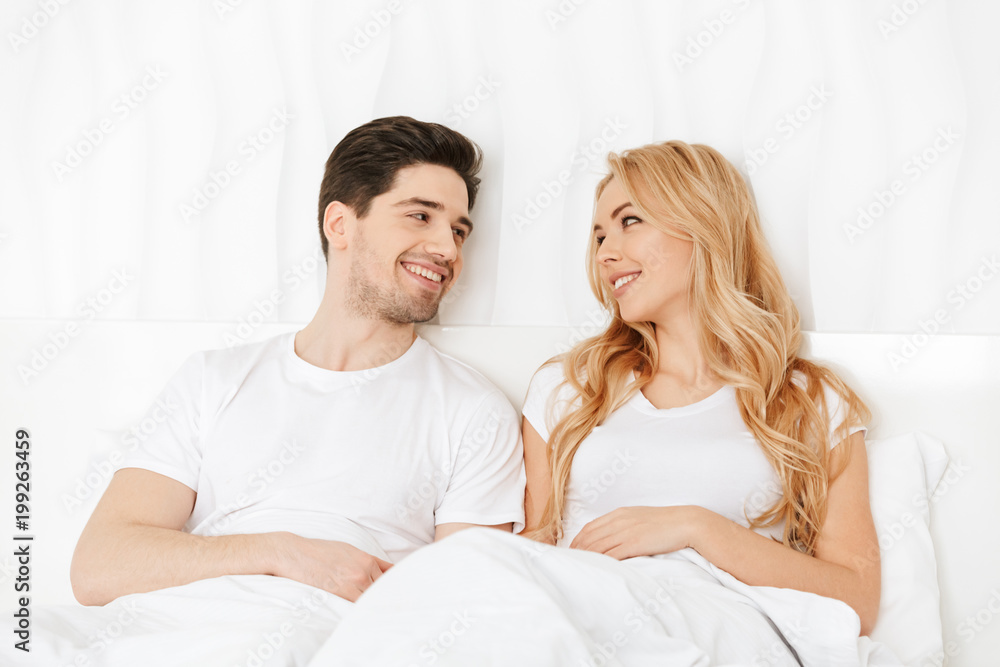 Loving couple lies in bed indoors at home.