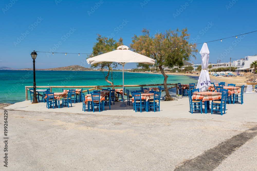 Tables with chairs in typical Greek tavern with view on sea bay near Agia Anna beach, Naxos Island. Greece.