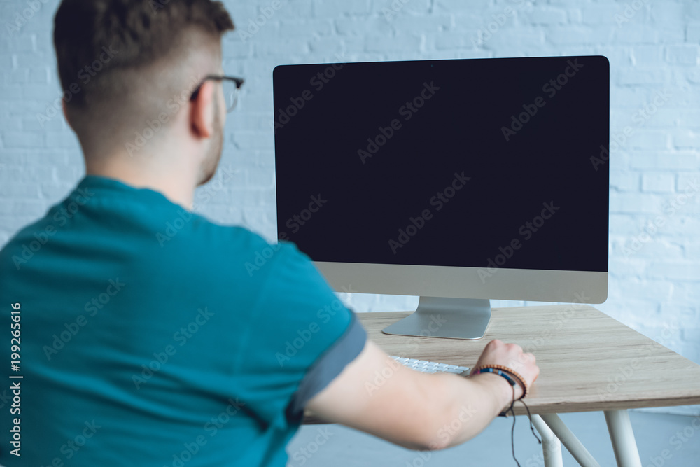 Rear view of man looking at computer screen on table Rear view of man looking at computer screen on table