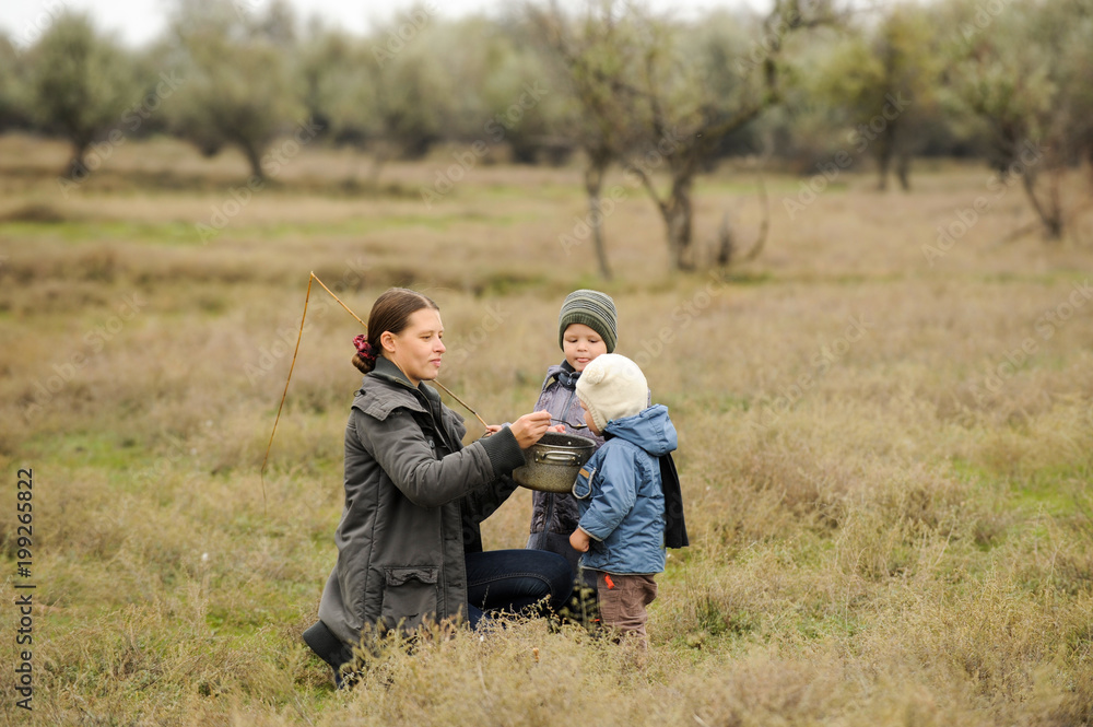 Young mother feeds her children with soup from pot outdoors outside house. concept of life in nature and happy rural childhood Young mother feeds her children with soup from pot outdoors outside house. concept of life in nature and happy rural childhood
