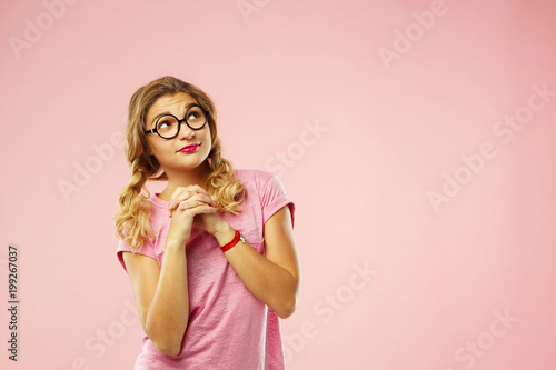 Portrait of a beautiful young woman in funny glasses looking up on copy space over pink background © Sunny