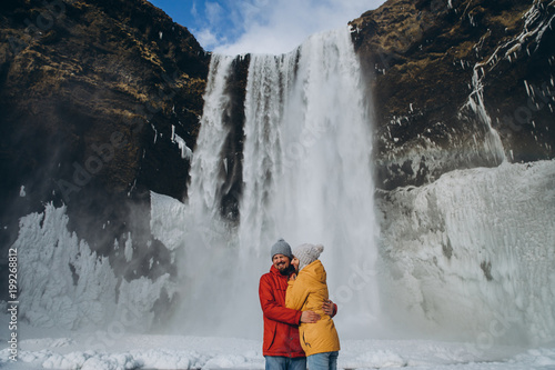 Fotografia happy young couple hugging near beautiful skogafoss waterfall in iceland