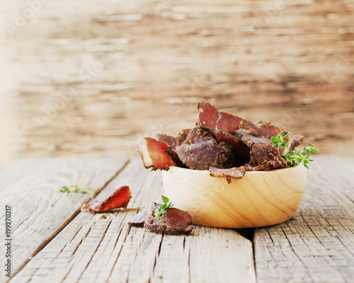jerked meat, cow, deer, wild beast or biltong in wooden bowls on a rustic table, selective focus