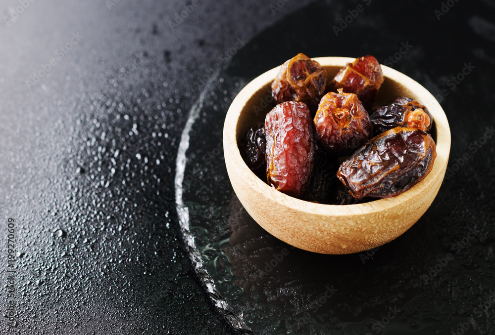 ripe dried dates in a wooden bowl on a black background close-up, selective focus ripe dried dates in a wooden bowl on a black background close-up, selective focus
