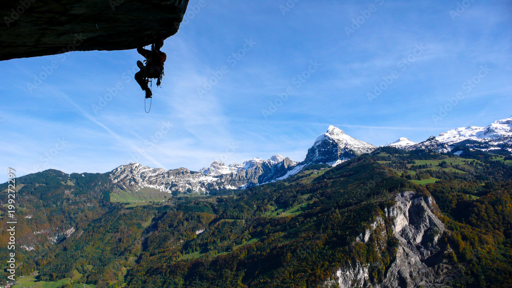 Obraz premium mountain guide on a large and overhanging roof lead and aid climbing a hard technical climb with a great background of blue sky and snow-capped peaks mountain landscape