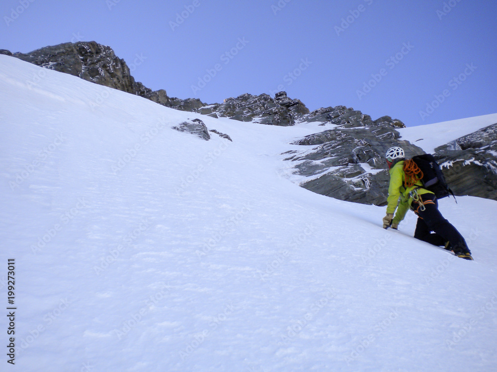 male mountain guide climbing a steep snow couloir on his way to a high summit in the Swiss Alps