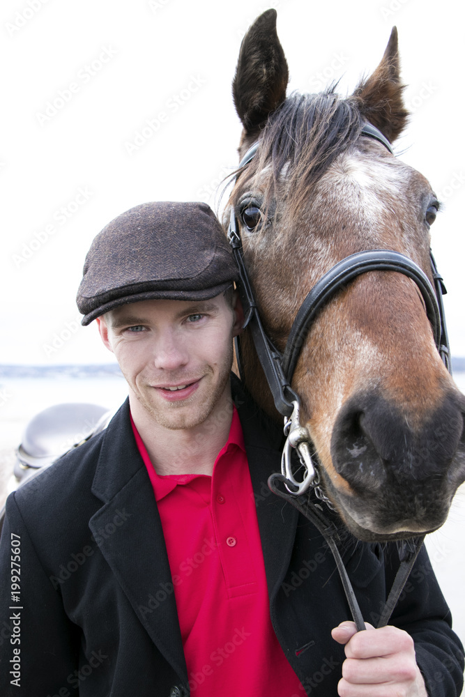 Fototapeta premium Portrait of horse rider and brown horse. He is wearing a flatcap, red polo shirt and black jacket