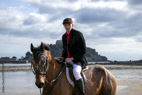 Handsome Male Horse Rider on horseback, wearing flat cap, white trousers and black boots