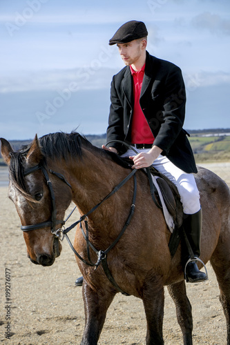 Handsome Male Horse Rider on horseback, wearing flat cap, white trousers and black boots