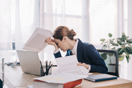 Photos overworked businesswoman in suit with papers in hands at workplace in office