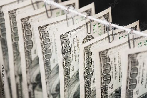 Fotografia Parts of hundred dollar bills hanging on clerical clips on a rope on the dark background