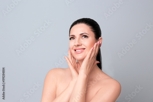 Beautiful woman with clean skin touching her face on light background