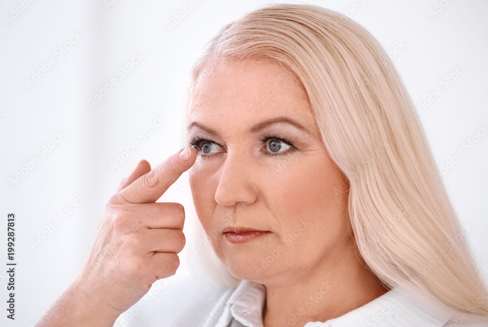 Senior woman putting contact lens in her eye on light background Senior woman putting contact lens in her eye on light background