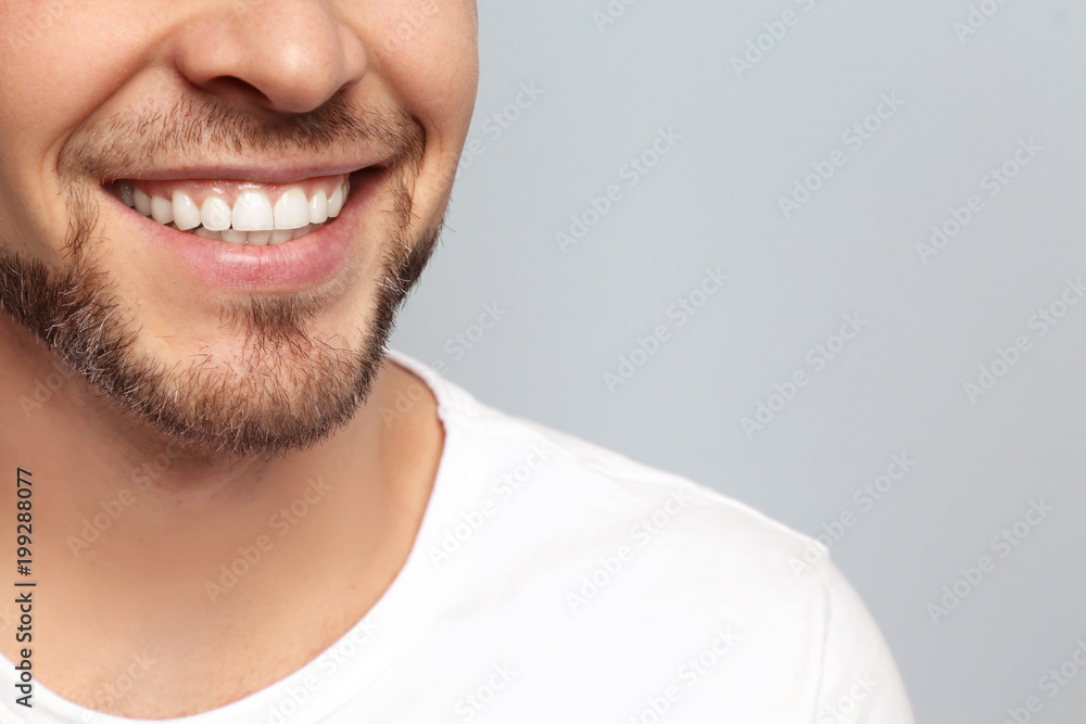 Young man with beautiful smile on grey background. Teeth whitening - obrazy, fototapety, plakaty 