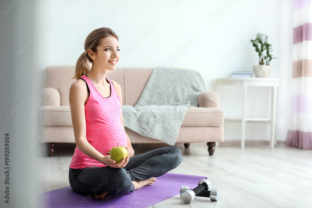 Young pregnant woman with apple at home