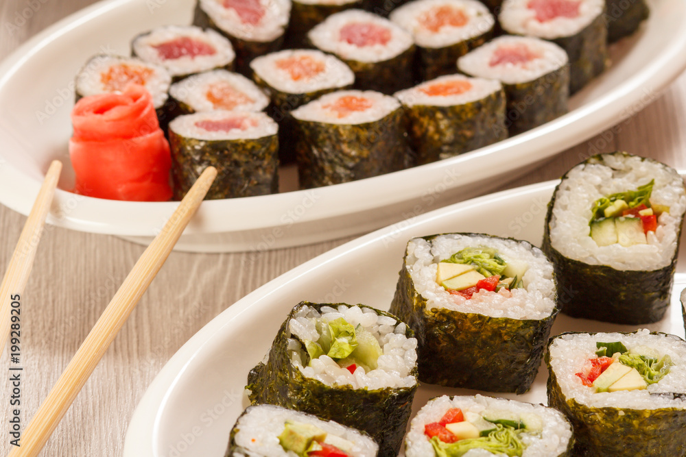 Sushi rolls with nori, rice, pieces of avocado, cucumber, red bell pepper and lettuce leaves on ceramic plate Sushi rolls with nori, rice, pieces of avocado, cucumber, red bell pepper and lettuce leaves on ceramic plate