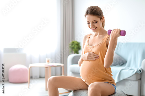 Young pregnant woman doing exercises with dumbbell at home