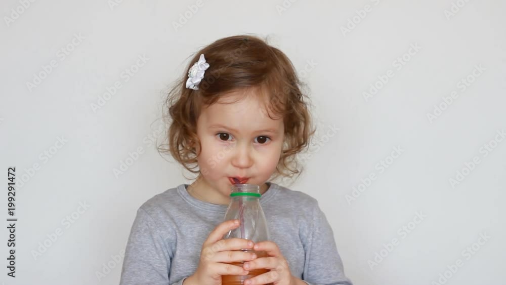 Little cute girl drinks orange drink from a bottle. Baby and freshly squeezed juice, smoothies, lemonade, fresh Little cute girl drinks orange drink from a bottle. Baby and freshly squeezed juice, smoothies, lemonade, fresh