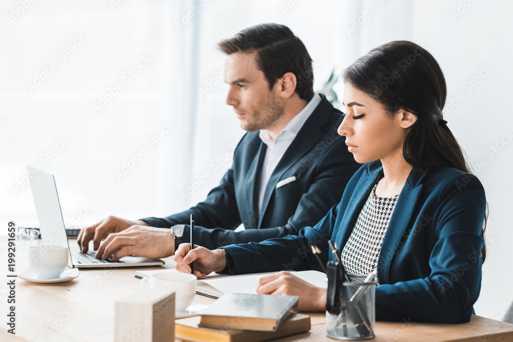 Business colleagues working by table with laptop in modern office