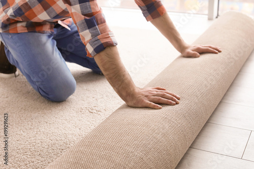 Fotografie Man rolling out new carpet flooring in room