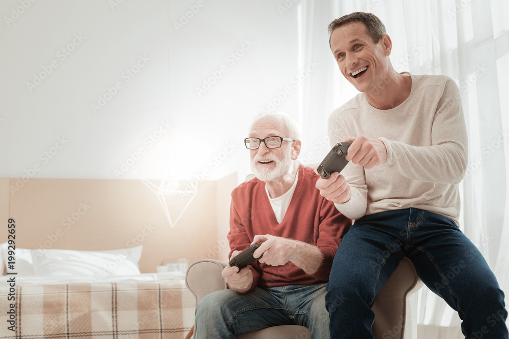 Modern entertainment. Occupied pleasant satisfied men sitting on the chair having fun and playing video games. Modern entertainment. Occupied pleasant satisfied men sitting on the chair having fun and playing video games.