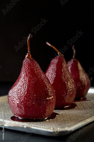 Pears in wine. Row of raditional dessert pears stewed in red wine on black background.
