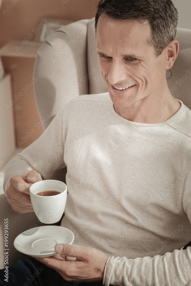 Adore these moments. Satisfied handsome calm man sitting on the chair having rest and drinking tea. Adore these moments. Satisfied handsome calm man sitting on the chair having rest and drinking tea.