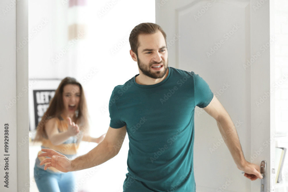 Young man walking out of door during argument with his girlfriend indoors Young man walking out of door during argument with his girlfriend indoors