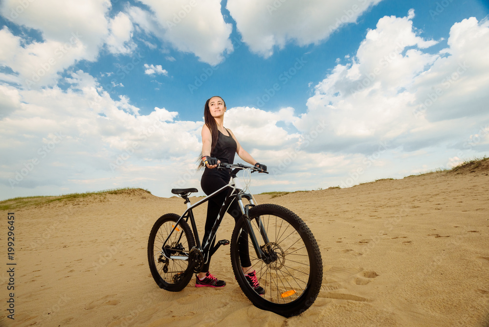 Bicyclist the summer sunset on the desert road in the reserve territory. Full length image of young female cyclist. Summer sunset. Bicycle and ecology lifestyle concept.