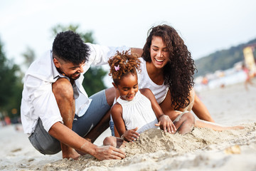 Young mixed race family sitting and relaxing at the beach on beautiful summer day.Playing in the sand.