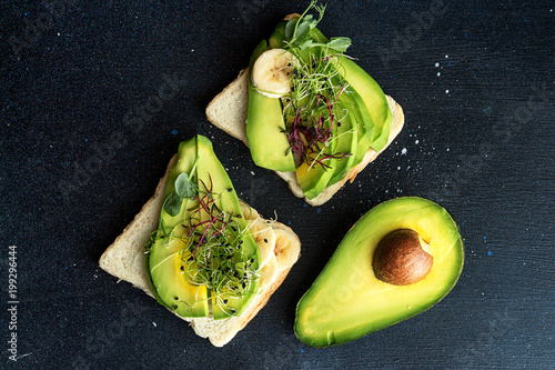 Healthy breakfast toasts with cream cheese, slices of avocado, banana and microgreen on dark background. Clean eating vegan dieting concept. T