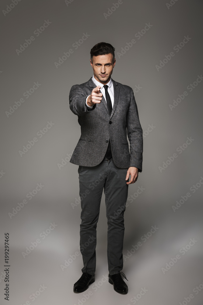 Full length portrait of caucasian businessman wearing business suit posing on camera and pointing finger on you, isolated over gray background Full length portrait of caucasian businessman wearing business suit posing on camera and pointing finger on you, isolated over gray background