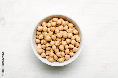 Chickpea in a white ceramic bowl on a wooden table, top view