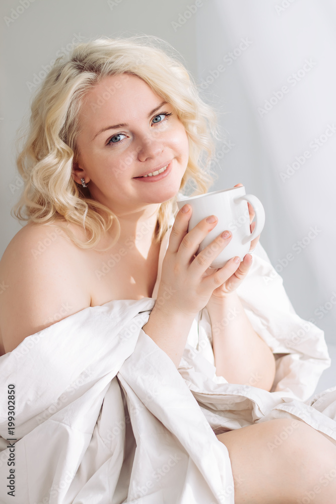Blonde caucasian girl drinking coffee blanket bed