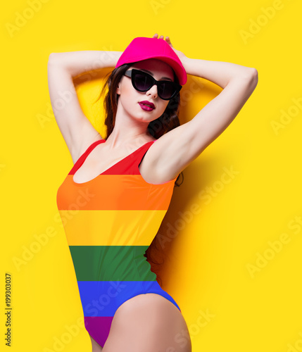 Elegant brunette woman in pink swimsuit and fashion cap. Sexy lady in pink beachwear, sunglasses enjoying sun on yellow summer background