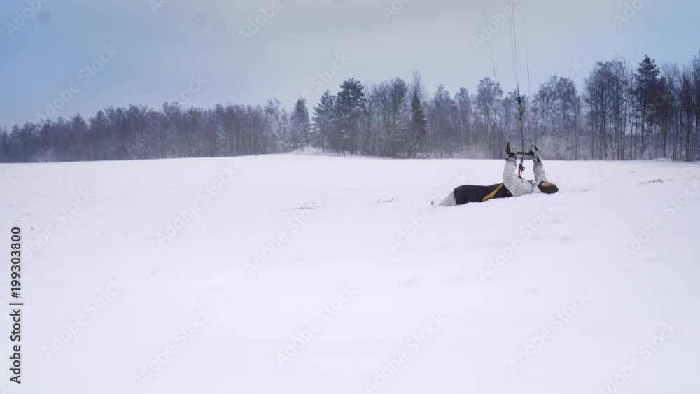 A man athlete dressed in sports outfit is engaged in snow kiting, then jumping and falling in snowdrift A man athlete dressed in sports outfit is engaged in snow kiting, then jumping and falling in snowdrift