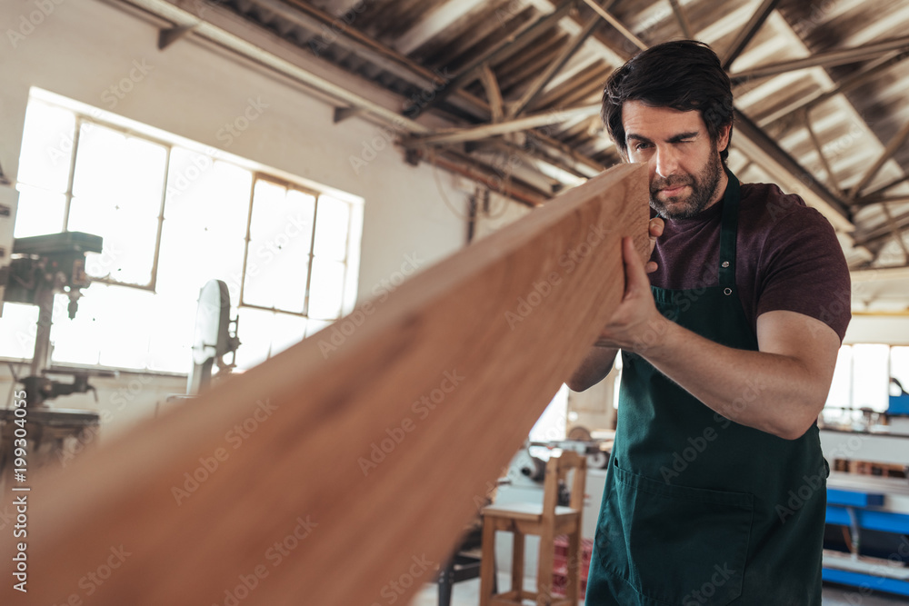 Skilled craftsman examining a plank of wood in his workshop Skilled craftsman examining a plank of wood in his workshop