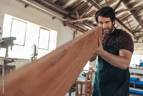 Canvas Print Skilled craftsman examining a plank of wood in his workshop