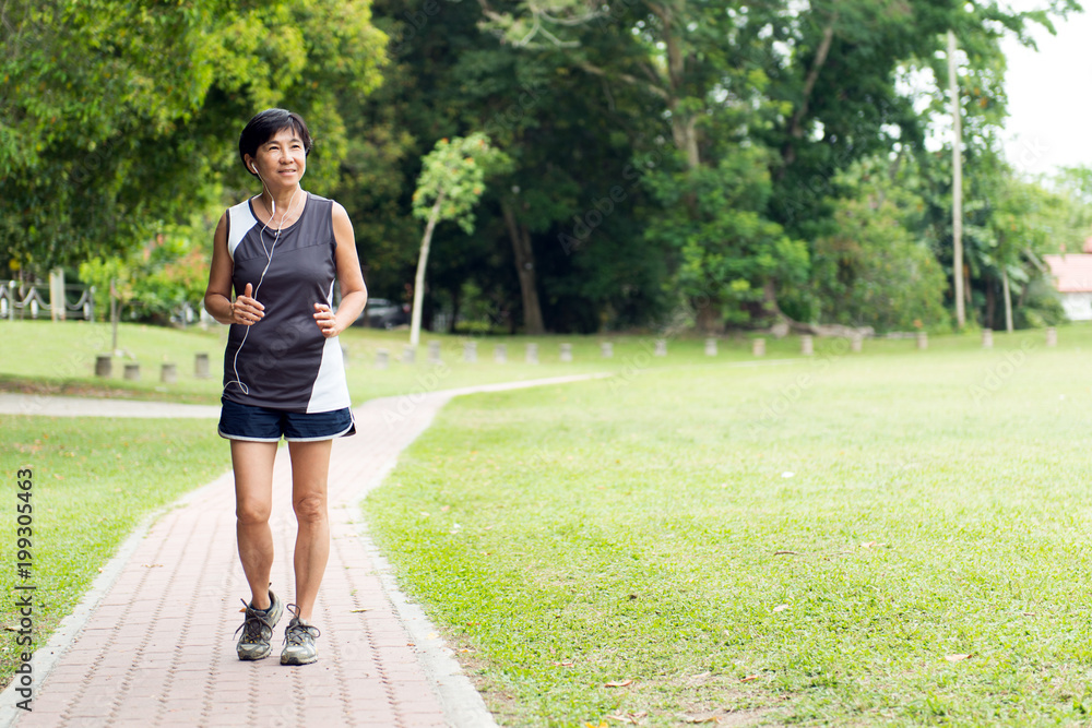 Front view of senior Asian woman jogging through park