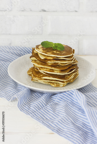 Stack of fresh baked pancakes with mint in white plate on blue linen on white background