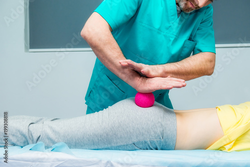 Woman at the physiotherapy receiving ball massage from therapist. A chiropractor treats patient's femur buttock in medical office. Neurology, Osteopathy, chiropractic. Selective focus, Close up.