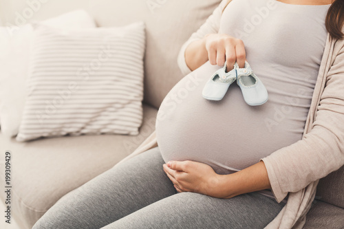 Fotografie Pregnant woman holding tiny shoes near belly