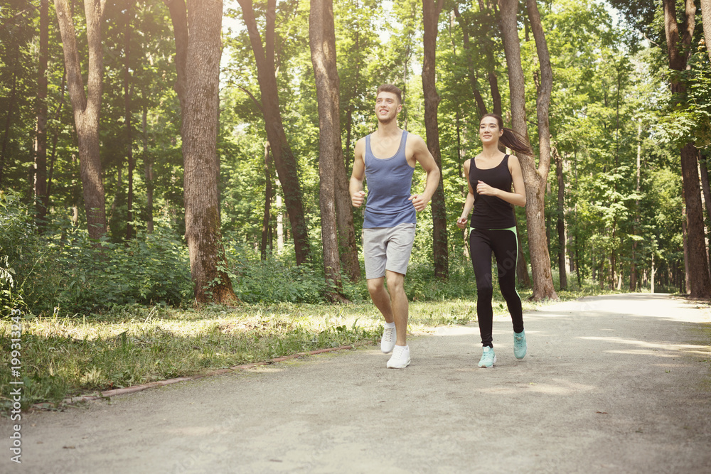 Young couple jogging in green park, copy space