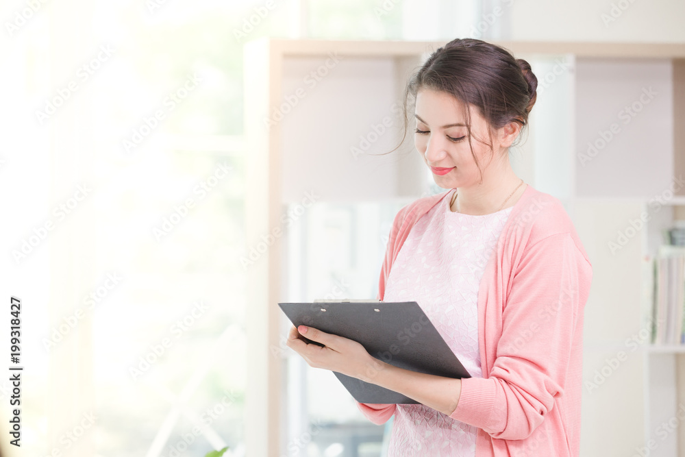 Business woman standing working near a window and holding clipboard at office. Business woman standing working near a window and holding clipboard at office.
