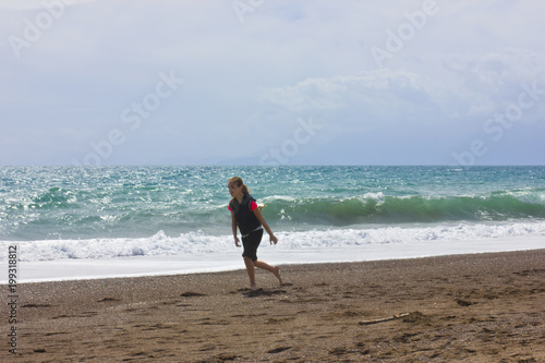 Young girl runs and jumps on the beach near the blue sea