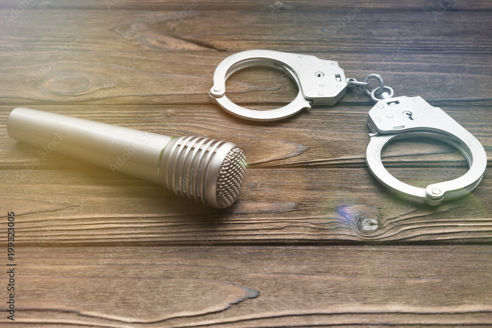 microphone, handcuffs on the background of a wooden table. copyright infringement. microphone, handcuffs on the background of a wooden table. copyright infringement.