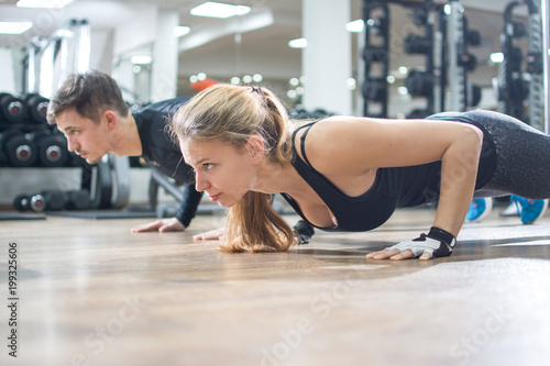 Sporty young woman and man doing push ups together in gym.