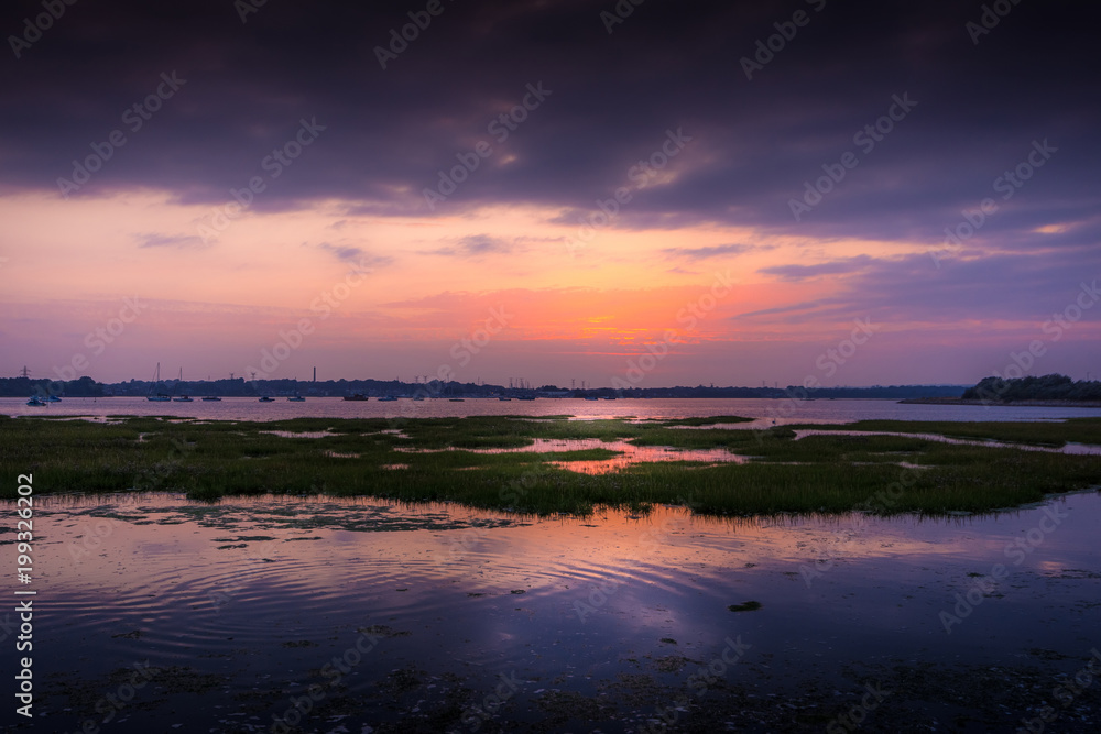 Beautiful warm sunset reflecting on calm water at Holes Bay in Poole, Dorset