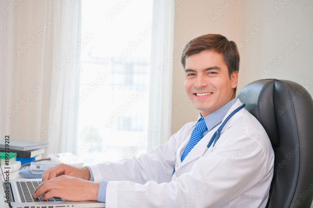 Smiling doctor posing in the office, he is wearing a stethoscope, medical staff on the hospital background